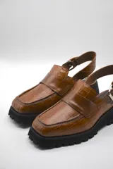 Zueco tipo mocasín color marrón con textura croco y tira regulable al talón.