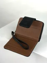 Billetera pequeña tipo clutch con correa de muñeca, confeccionada en cuero negro texturizado y un panel central de pelo (pellejo) en tonos blanco y negro. Presenta costuras blancas de contraste y un cierre de solapa con broche.