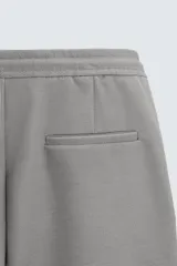 Bermuda color crudo de corte recto, con cintura elástica ajustable con cordón, pliegues frontales, bolsillos laterales y bolsillos traseros de vivo.