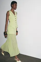 Falda midi color crudo, de tiro alto con cintura elástica y detalle de tejido combinado plisado y semitransparente. Cierre lateral con cremallera oculta en costura.