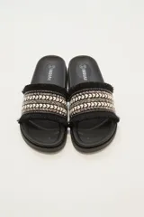 Sandalias tipo slider blancas, con tira ancha decorada con trenzado de hilo beige y plateado, tachas piramidales plateadas y flecos blancos en los bordes.