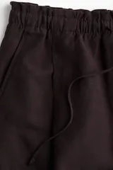 Short marrón de lino con cintura elastizada y cordón ajustable. Presenta pliegues frontales, bolsillos laterales y corte holgado.