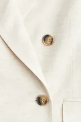 Blazer color crema de lino con doble botonadura, solapas de muesca y bolsillos delanteros ribeteados con solapa. Forrado.