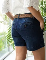 Short de jean azul oscuro con pretina con pasadores, botón y cierre. Delantera con bolsillos. Botón en bolsillos traseros. Incluye cinturón trenzado marrón con hebilla redonda dorada.