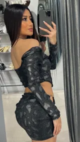 Conjunto negro brillante con estampado animal print, compuesto por un top de mangas largas con escote cuadrado y una minifalda con detalle de aro metálico en la cadera.