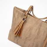 Bolso tote color marrón claro con textura tipo arpillera, doble asa fina color camel y detalle de borla decorativa.