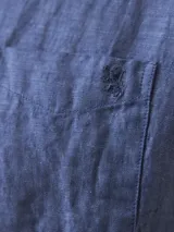 Camisa azul de lino con botones blancos, manga larga y bolsillo en el pecho.