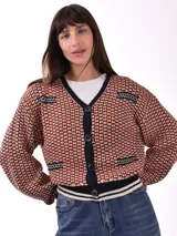 Cárdigan tejido con patrón geométrico en tonos naranja, negro y blanco. Tiene cuello en V, cierre con botones negros y ribetes a contraste en cuello, puños y bajo.