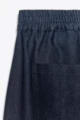 Pantalón de denim azul oscuro, de tiro medio y corte ancho, con cintura elástica en la parte trasera y cierre frontal con cremallera y botón.