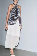 Falda midi color blanco, semitransparente, de tiro medio con cintura elástica, forro corto interior y abertura en la espalda.