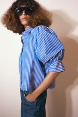 Camisa de cuello redondo con estampado de rayas verticales azules y blancas, manga larga abullonada y cierre frontal con botones.