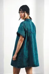 Vestido corto de denim celeste con cuello tipo camisa, cierre frontal metálico y bolsillos delanteros. Presenta bordados de soles y lunas en el canesú delantero y trasero.