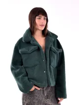 Campera corta color verde petróleo, de textura suave tipo peluche, con cuello camisero, cierre con botones a presión, dos bolsillos de parche en el pecho y mangas largas.