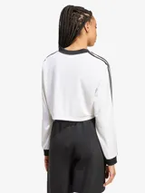 Top corto blanco de manga larga con cuello en V y ribete negro. Presenta las tres rayas características de Adidas en las mangas y el logo bordado en el pecho.