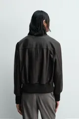 Cazadora estilo bomber cropped fit de piel negra, con cuello solapa, cierre frontal de cremallera, bolsillos frontales de plastrón con solapa y puños y bajo de rib elástico ancho.