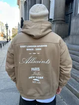 Canguro tostado de algodón con capucha, puños y cintura acanalados. Estampado en la espalda con la frase "East London Studios Since 1994", el logo de Allsaints y nombres de ciudades.