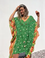 Túnica corta verde con estampado de flores blancas y detalles bordados en el escote. Mangas anchas con terminación en tela estampada a rayas naranjas y blancas.