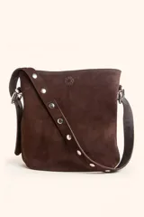 Cartera tipo balde de gamuza color marrón, con correa ajustable decorada con tachas metálicas plateadas y logo grabado en la parte frontal.