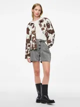 Chaqueta de jean con estampado animal print de vaca en tonos marrones y blancos, corte recto, cuello camisero y cierre frontal con botones.