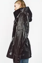 Parka marrón brillante con cuello alto y capucha oculta con cremallera metálica. Manga larga ajustable con cinta y botones a presión. Bolsillos delanteros con cremallera metálica. Cintura ajustable. Cierre frontal con cremallera y botones a presión.