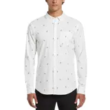 Camisa blanca de manga larga con estampado de palmeras y aves pequeñas en tonos naranja y azul. Tiene cuello abotonado, bolsillo en el pecho y corte clásico.