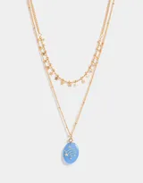 Collar corto dorado multicadena con dije ovalado celeste con estrellas y dijes de estrellas colgantes.