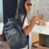 Mochila de eco-cuero color negro, con diseño estructurado y múltiples compartimentos frontales con cierre. Posee correas ajustables para llevar al hombro.