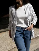 Blazer blanco con rayas verticales negras, cuello con solapa, bolsillos simulados y mangas 3/4 fruncidas. Forro interno blanco, marca Dictionary.