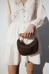 Bolso mini trenzado color marrón con asa de mano dorada metálica y doble asa bandolera ajustable y extraíble. Tiene forro, bolsillo interior y cierre mediante cremallera.