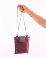 Porta celular de cuero color bordó con correa de cadena plateada, solapa con broche y tachas plateadas en los bordes.