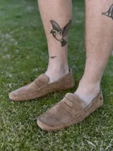 Mocasín de cuero gamuzado color marrón claro, con punta redonda y detalle de costuras a la vista.