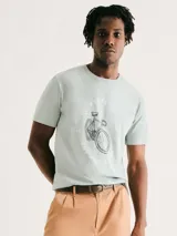 Camiseta blanca de algodón con cuello redondo y mangas cortas. Estampa rectangular con borde negro que contiene la frase "NATURAL ATMOSPHERE" en letras mayúsculas y una imagen de montañas y mar.