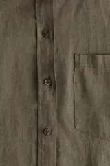 Camisa verde militar de lino liviano con cuello, botones adelante y canesú de doble capa en la espalda. Modelo con hombros apenas caídos, mangas largas con puños abotonados, bolsillo superior de parche y bajo levemente redondeado.