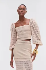 Top cropped color beige, tejido a crochet con mangas abullonadas 3/4, escote cuadrado y cierre con cremallera en la espalda.