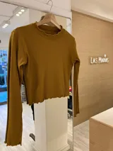 Remera gris de morley de algodón, de manga larga, con terminaciones fruncidas en cuello y mangas.