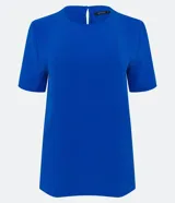 Blusa blanca de poliéster con cuello redondo, mangas cortas, cierre trasero en forma de gota, pequeñas aberturas laterales y acabados en pespuntes en las mangas y el cuello.