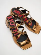 Sandalias de cuero charol color borgoña con tiras finas, taco cuadrado bajo y cierre con hebilla en el tobillo. Interior con estampado del logo de la marca en color naranja.