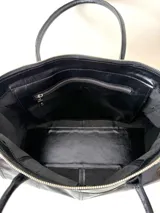 Bolso grande de cuero marrón con textura tipo cocodrilo, estructura rígida y asas para llevar al hombro. Tiene una tira con tachas y hebillas en cada extremo, también lleva lazos en los costados.