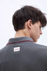 Chomba blanca de algodón con cuello clásico, media cartera de botones, bordado con la palabra 'Uniform' en el pecho y puños con rayas azul marino y rojo.