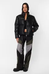 Campera puffer negra de cuerina PU opaca, corte boxy fit, cuello alto con elástico y tancas metálicas, acceso delantero con cierre metálico desmontable y tiracierre de marca, bolsillos ribete con snap metálico y bolsillo superior con cierre metálico cubierto por vista y avío marcario, mangas desmontables por cierre de nylon cubierto con vista, terminaciones de mangas y cintura con elástico interno, forrería al tono, cinta gross estampada nombre de marca y snaps en sus extremos para transportarla al hombro, bolsillo interno de tela base con cierre invisible.