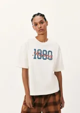 Camiseta beige de corte amplio con estampa frontal con el texto "1880 Hering" en azul y rojo.