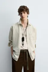 Camisa de hombre relaxed fit confeccionada en tejido de algodón a rayas verticales color beige y marrón. Tiene cuello solapa, manga larga con puños abotonados, bolsillo de parche en el pecho y cierre frontal con botones.