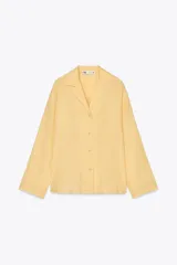 Camisa de lino color amarillo claro, de corte recto, con cuello solapa, escote en pico, cierre frontal con botones y mangas largas con puños abotonados.