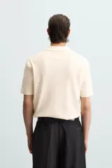 Polo color crema de punto, corte regular fit, con cuello solapa y abertura frontal.