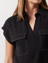 Blusa negra con cuello con solapa y escote en V, con bolsillos delanteros y pespuntes blancos.