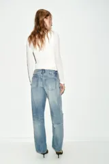 Jeans de tiro bajo, corte recto y pierna ancha, color celeste claro desgastado. Presenta roturas visibles en la zona de la rodilla y pequeños desgastes en los muslos y bolsillos.