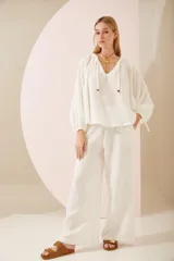 Camisa oversize blanca de lino, con cuello en V, mangas largas abullonadas con puños elásticos y lazos decorativos.