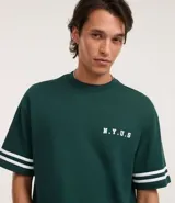 Remera de algodón color verde oscuro, corte relaxed, cuello redondo y manga corta. Presenta un pequeño estampado en el pecho con el texto "N.Y.U.S" en blanco y dos franjas blancas horizontales en cada manga.
