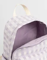 Mochila de tela con estampado a cuadros lila y blanco, con bolsillo frontal con cierre y moño bordado. Tiene correas regulables, manija superior y doble cierre superior.