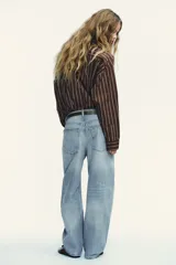 Pantalón de jean azul oscuro, tiro medio, corte amplio tipo baggy balloon con costuras torcidas y cinco bolsillos. Cierre frontal con cremallera y botón metálico.